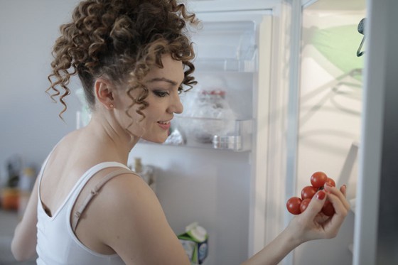 a woman gets a handful of tomatoes from the fridge